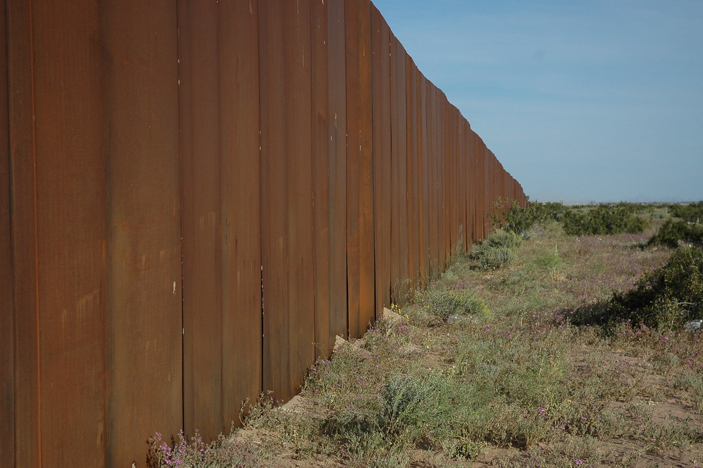 "I hope someone tears down The Wall, US border, separating Mexico from the US, looking east, along Highway 2, Sonora Desert, Mexican side" by Wonderlane is licensed under CC BY 2.0.